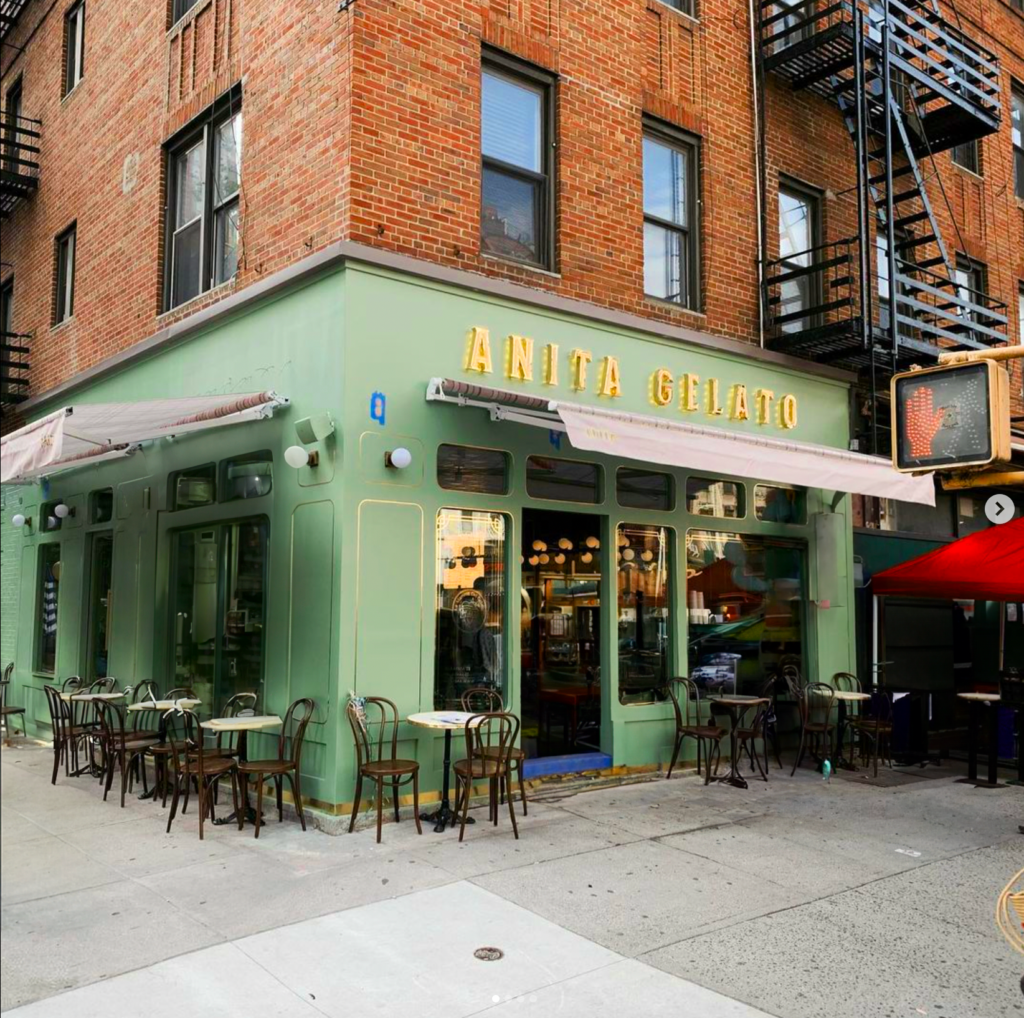 A green building with a red umbrella and outdoor tables.
