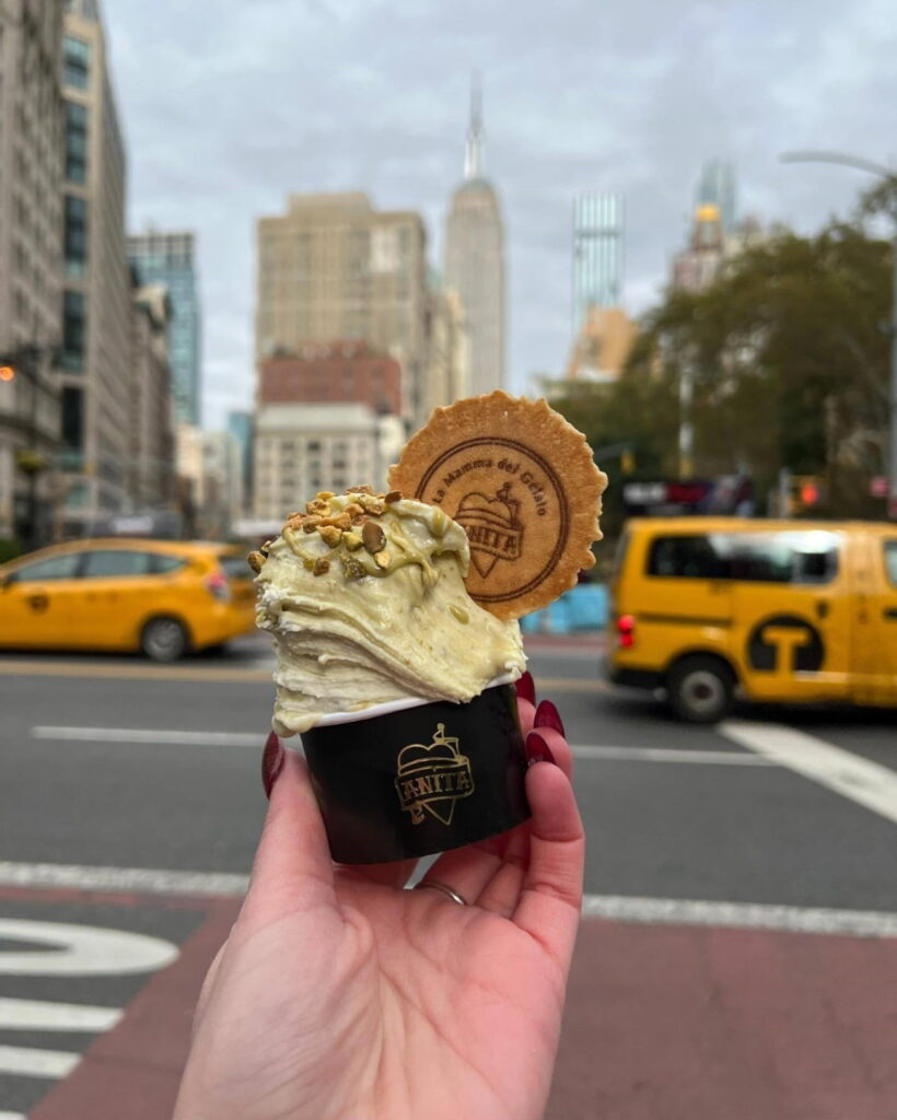 Person holding cup of ice cream with cookie atop.