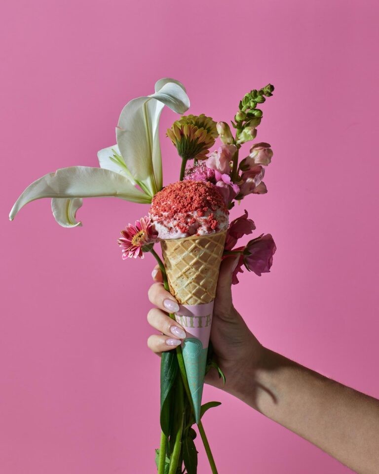 someone holding a cone with flowers in it on a pink background