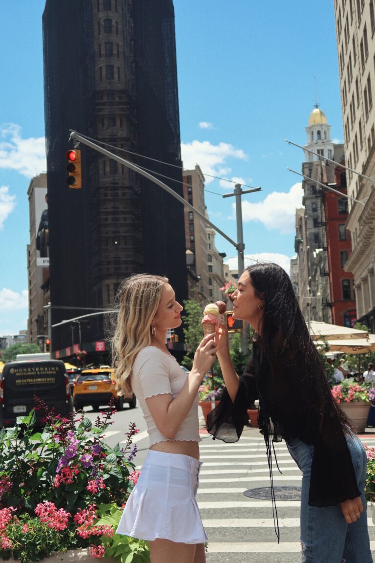 Two women standing on the street eating donuts.