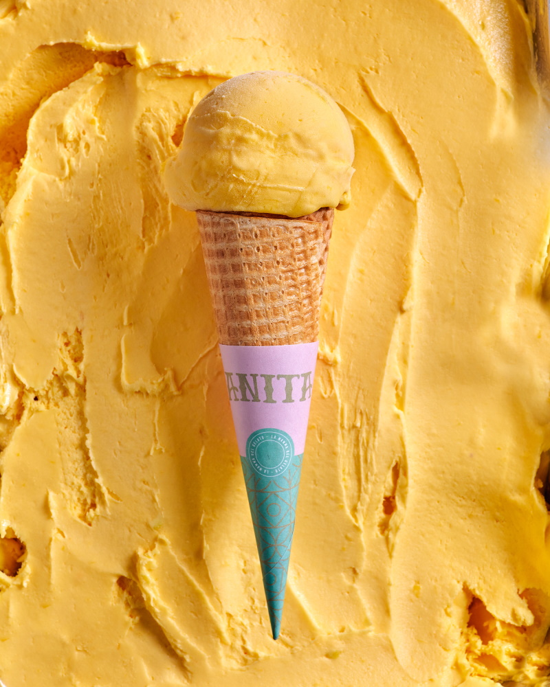 Yellow ice cream in a cone with a blue cone sticking out of it.
