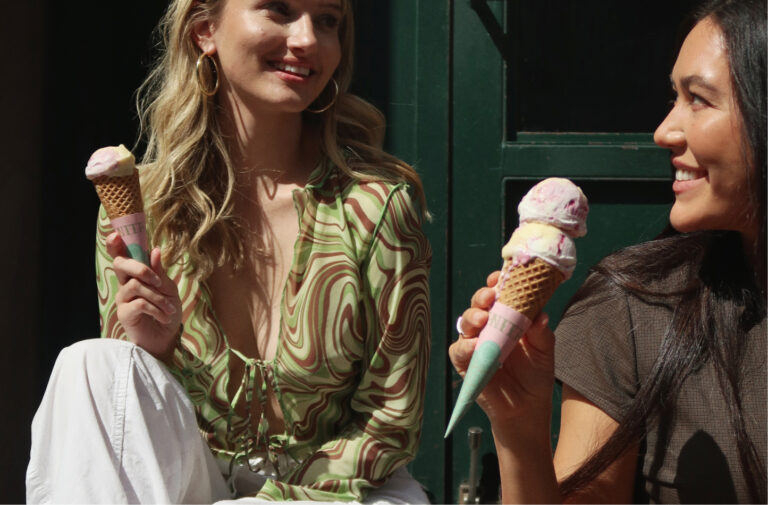 Two women eating ice cream cones on a bench.