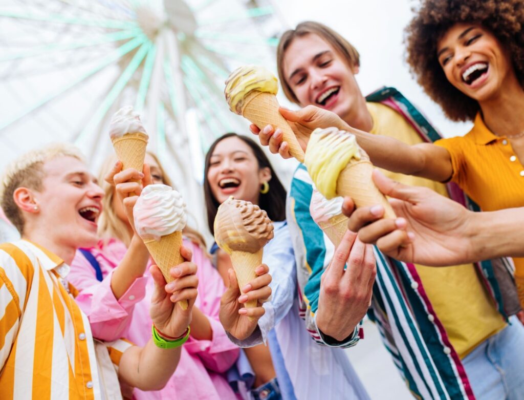 several people are holding up ice cream cones in front of a ferris wheel